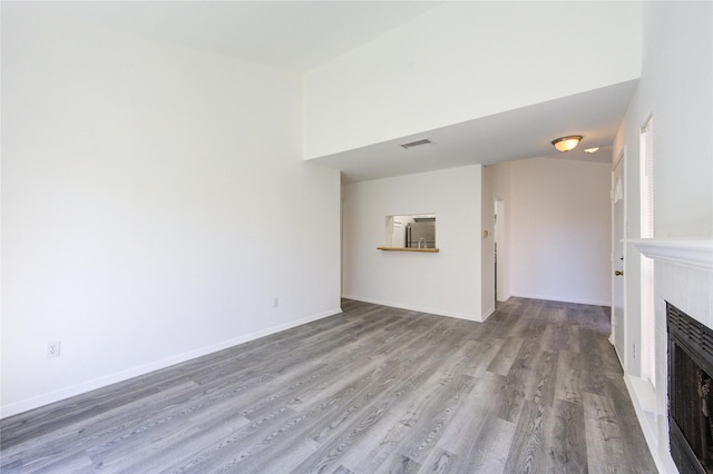 unfurnished living room featuring a fireplace, heating unit, visible vents, wood finished floors, and baseboards