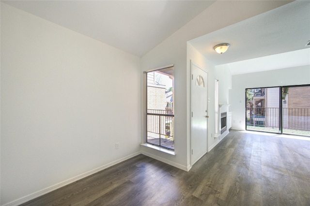 empty room with dark wood-style floors, a fireplace, baseboards, and vaulted ceiling