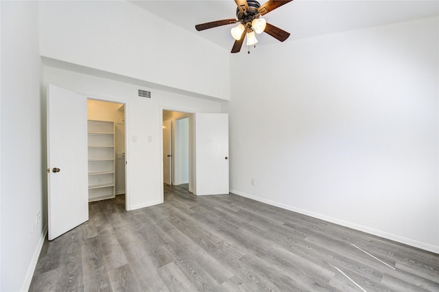 unfurnished bedroom featuring a walk in closet, visible vents, a high ceiling, wood finished floors, and baseboards