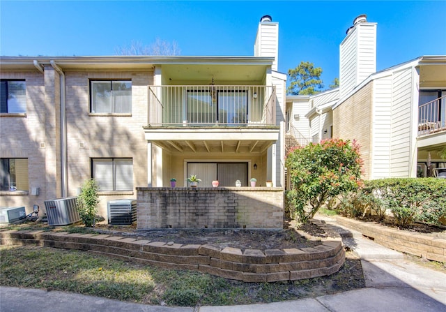 exterior space with central AC unit, a balcony, and brick siding