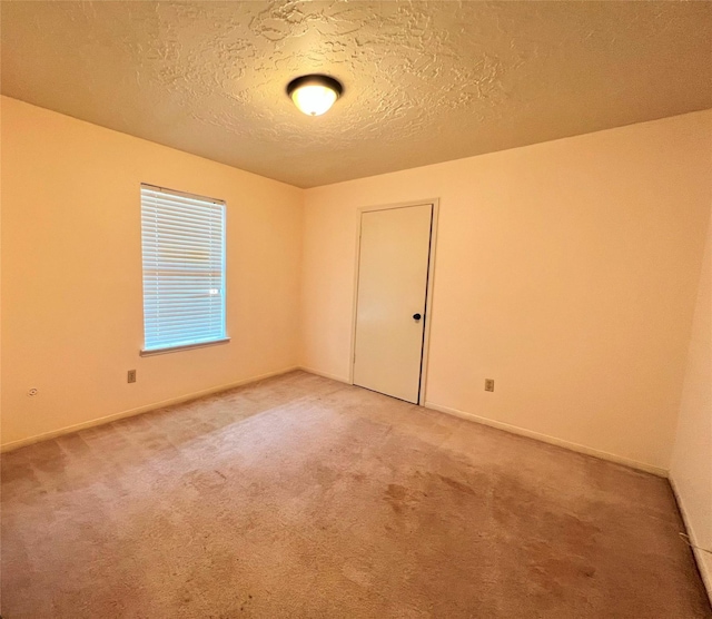 empty room featuring light carpet, baseboards, and a textured ceiling