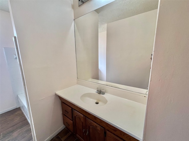 bathroom featuring a bathtub, vanity, wood finished floors, baseboards, and walk in shower