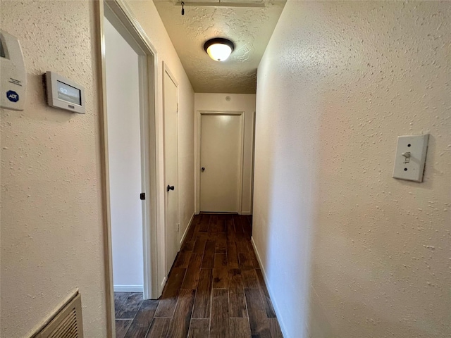 hallway featuring a textured ceiling, a textured wall, and wood tiled floor