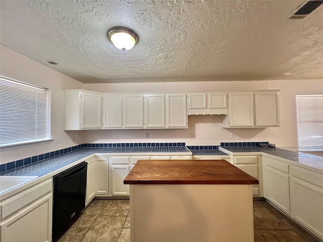 kitchen with a kitchen island, visible vents, white cabinets, black dishwasher, and wooden counters