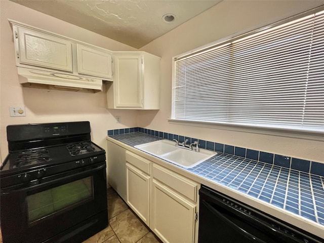 kitchen with tile counters, white cabinetry, a sink, under cabinet range hood, and black appliances