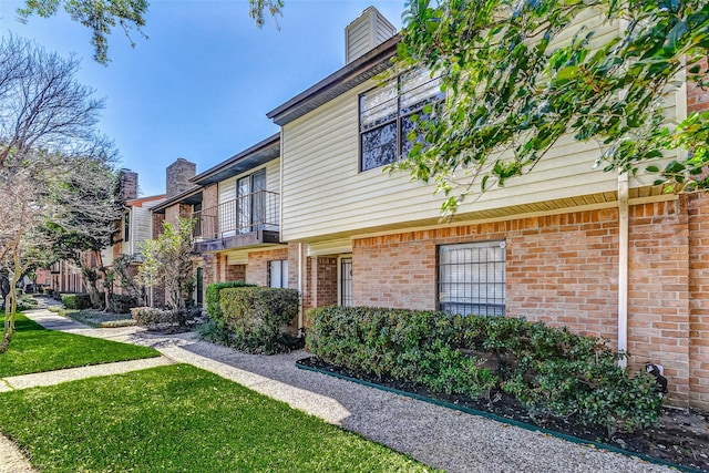 view of side of home featuring a balcony, a yard, a chimney, and brick siding