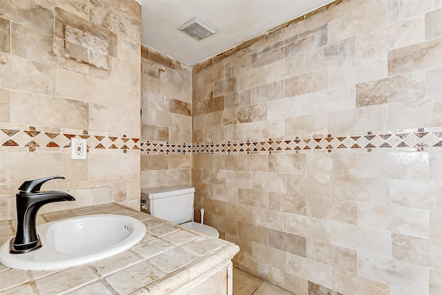 bathroom featuring toilet, a sink, visible vents, and tile walls