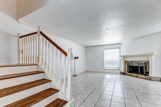 unfurnished living room featuring light tile patterned flooring, a tile fireplace, baseboards, ornamental molding, and stairway