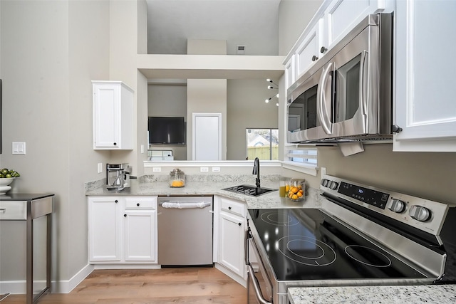 kitchen with light stone counters, stainless steel appliances, white cabinetry, a sink, and light wood-type flooring