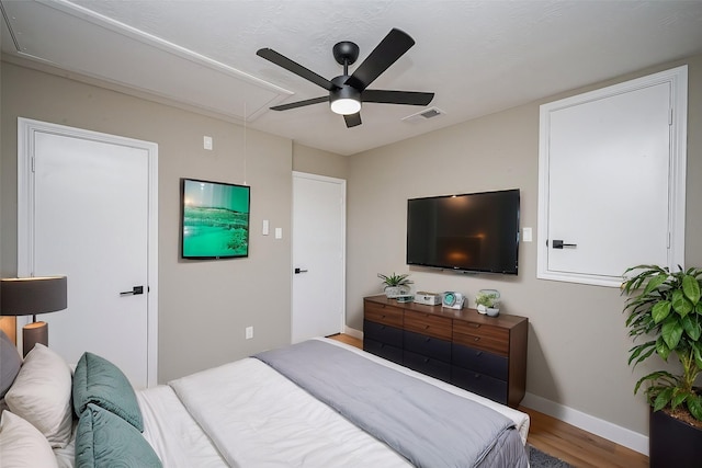 bedroom with attic access, baseboards, visible vents, ceiling fan, and wood finished floors