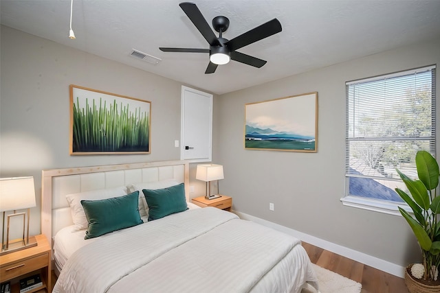 bedroom with a ceiling fan, visible vents, baseboards, and wood finished floors