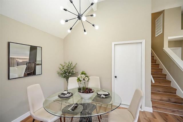 dining space featuring a notable chandelier, lofted ceiling, stairway, wood finished floors, and baseboards