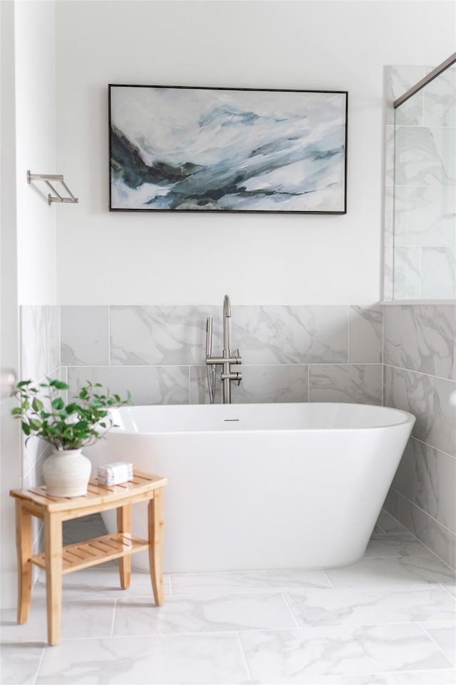 bathroom featuring marble finish floor, a freestanding bath, and tile walls