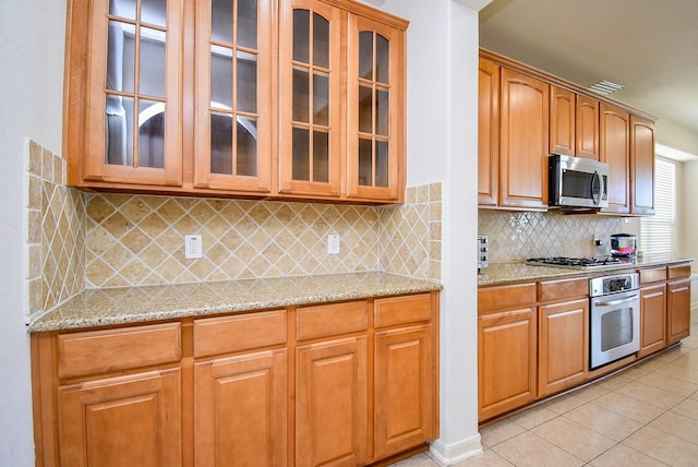 kitchen featuring glass insert cabinets, light stone countertops, appliances with stainless steel finishes, and light tile patterned flooring