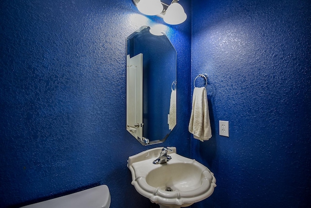 bathroom with a textured wall, a sink, and toilet