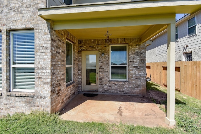 view of exterior entry featuring a patio, brick siding, and fence