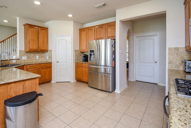 kitchen featuring light tile patterned floors, arched walkways, a sink, visible vents, and stainless steel fridge