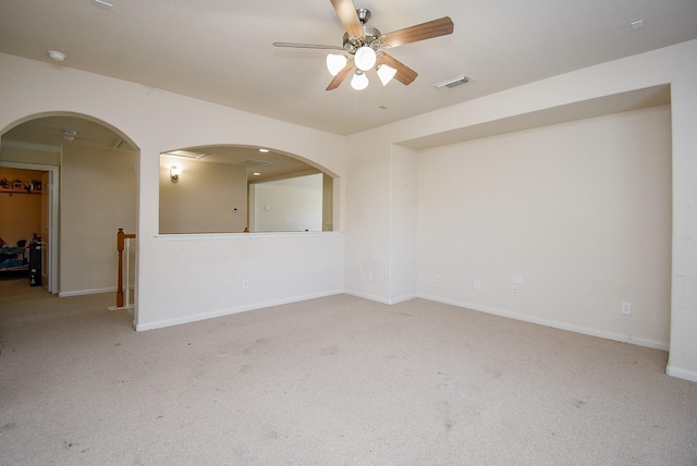 carpeted spare room featuring baseboards, visible vents, arched walkways, and a ceiling fan