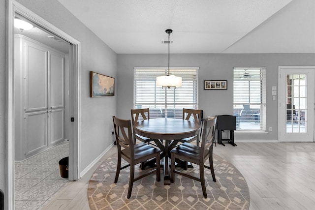 dining space featuring baseboards, vaulted ceiling, visible vents, and light wood-style floors