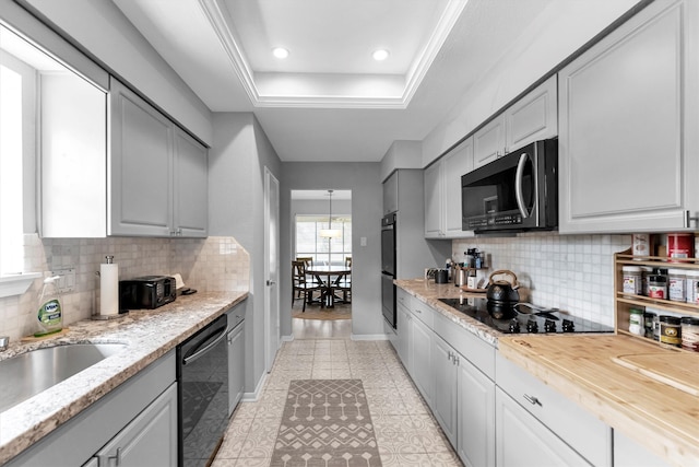 kitchen featuring light tile patterned floors, baseboards, backsplash, black appliances, and a tray ceiling