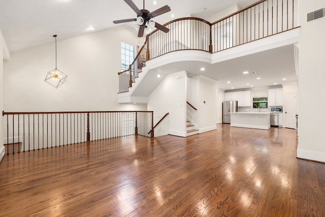 unfurnished living room featuring visible vents, a high ceiling, wood finished floors, baseboards, and ceiling fan with notable chandelier