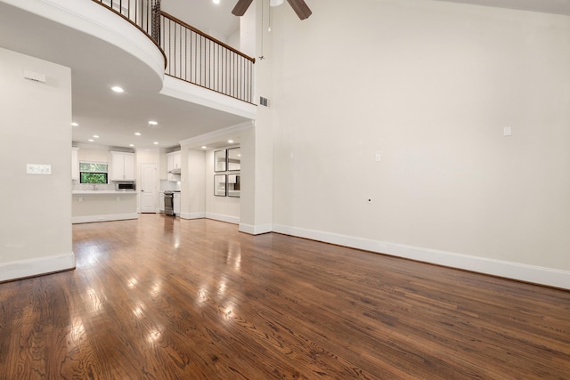 unfurnished living room with visible vents, baseboards, a towering ceiling, ceiling fan, and dark wood-type flooring