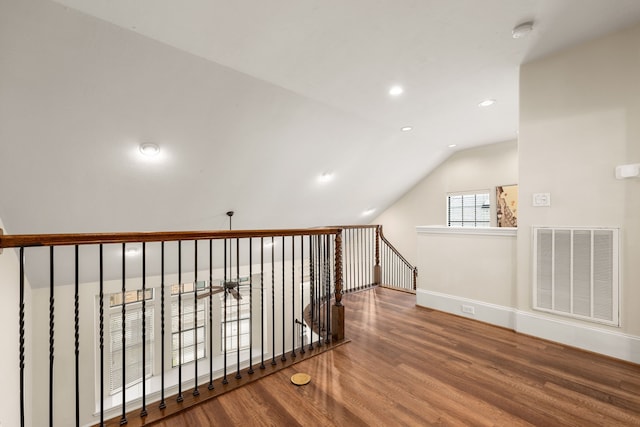 corridor with lofted ceiling, an upstairs landing, wood finished floors, and visible vents