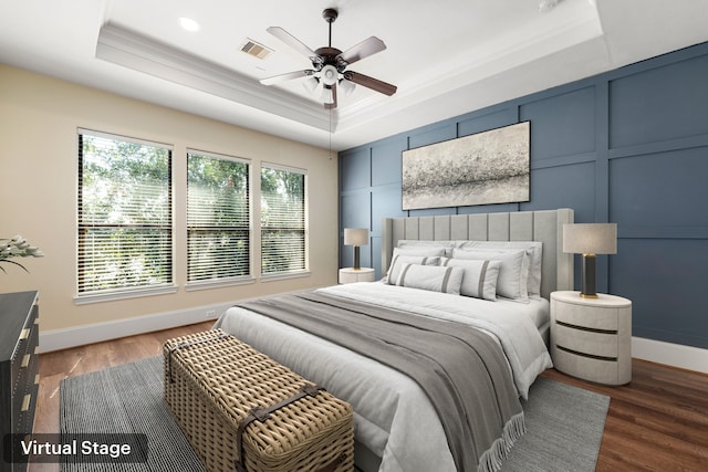 bedroom with a raised ceiling, wood finished floors, and a decorative wall