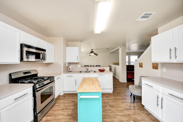 kitchen featuring a peninsula, butcher block counters, a sink, visible vents, and appliances with stainless steel finishes