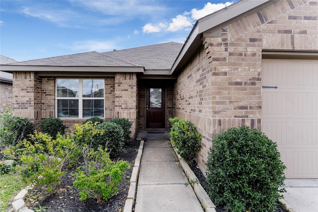 doorway to property featuring a garage, brick siding, and roof with shingles