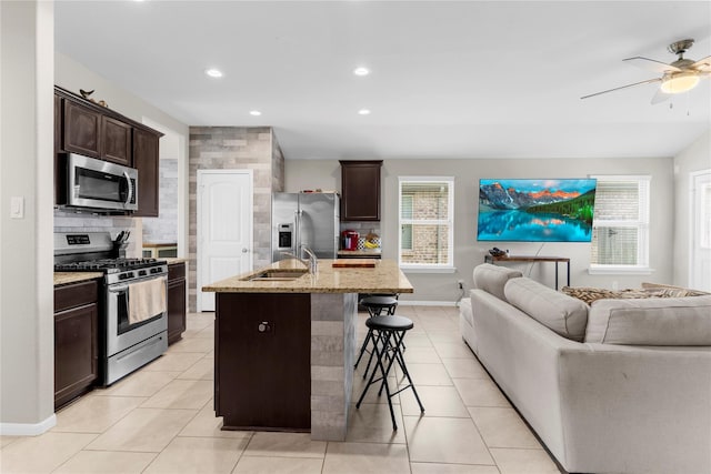 kitchen with dark brown cabinetry, stainless steel appliances, a breakfast bar, a sink, and open floor plan