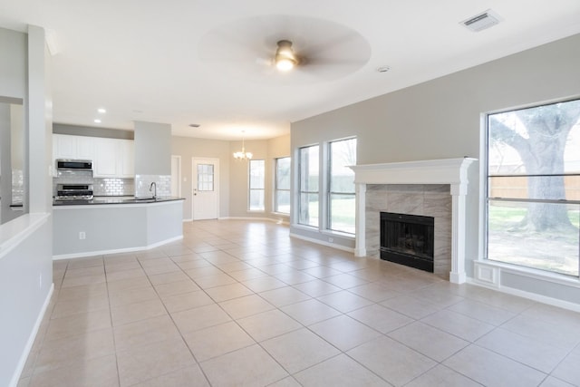 unfurnished living room with light tile patterned flooring, ceiling fan with notable chandelier, a fireplace, visible vents, and baseboards