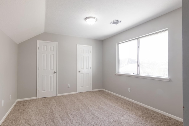 unfurnished bedroom with vaulted ceiling, carpet, visible vents, and baseboards