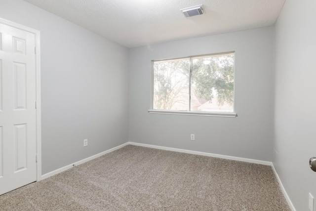 empty room with a textured ceiling, carpet flooring, visible vents, and baseboards