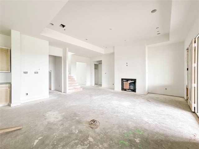 unfurnished living room featuring concrete flooring, a tray ceiling, and stairway