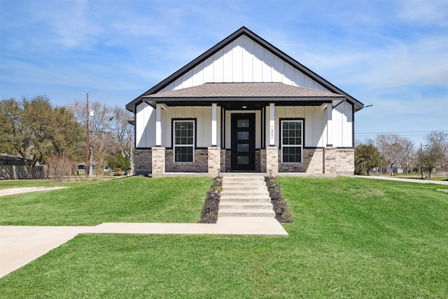 view of front facade featuring brick siding, a shingled roof, covered porch, board and batten siding, and a front yard