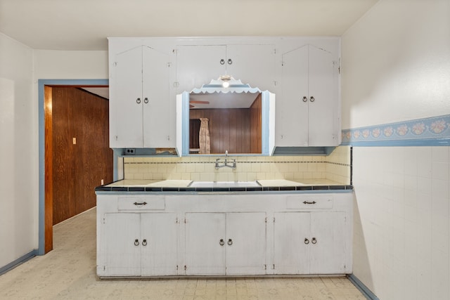 kitchen featuring tile walls, a sink, tile counters, and white cabinetry