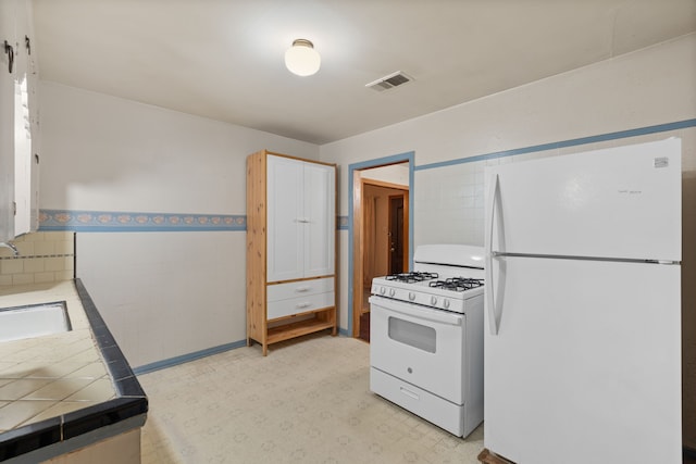 kitchen featuring tile countertops, white appliances, visible vents, tile walls, and light floors