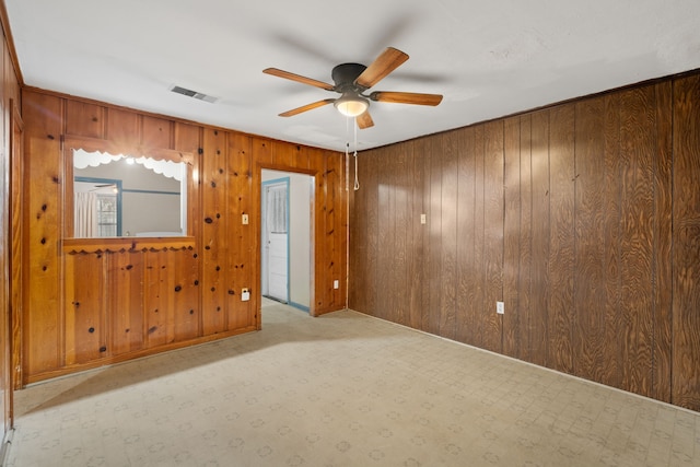 spare room with ceiling fan, wooden walls, and visible vents