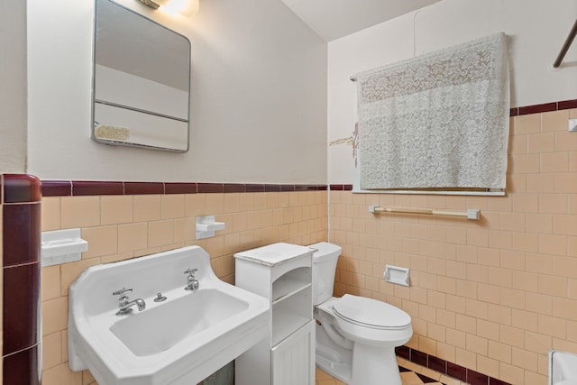 bathroom with tile patterned flooring, toilet, a sink, tile walls, and wainscoting