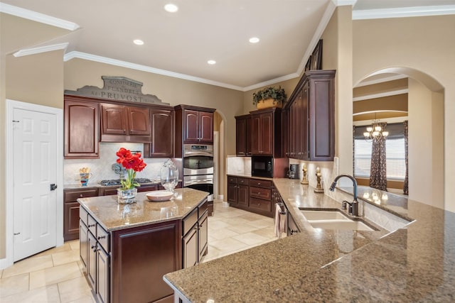 kitchen with arched walkways, a center island, decorative backsplash, appliances with stainless steel finishes, and a sink