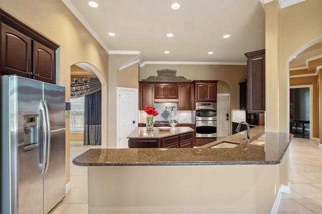 kitchen featuring stainless steel appliances, arched walkways, dark stone counters, and a sink