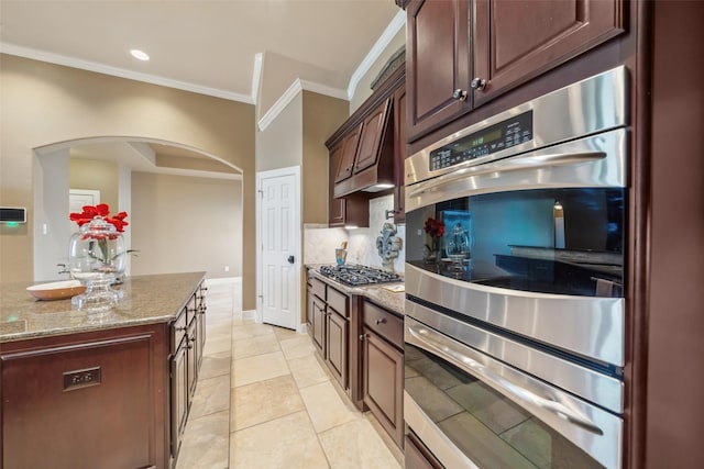 kitchen featuring arched walkways, light stone counters, ornamental molding, stainless steel double oven, and backsplash