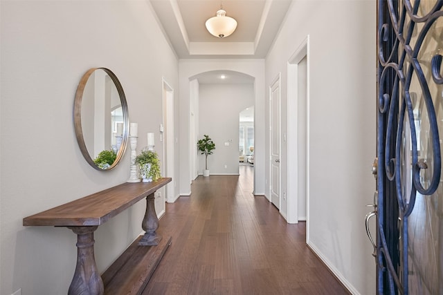 foyer entrance featuring plenty of natural light, baseboards, arched walkways, dark wood-type flooring, and a tray ceiling