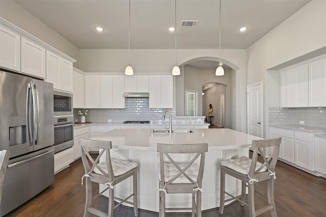 kitchen with arched walkways, dark wood-style flooring, visible vents, appliances with stainless steel finishes, and a sink