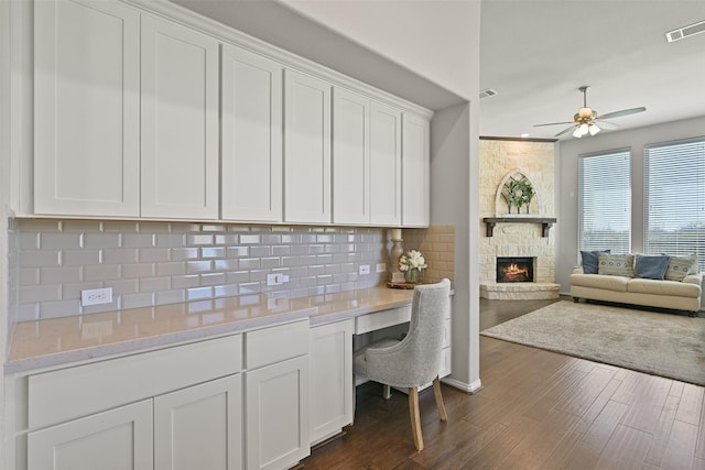 interior space featuring dark wood-style flooring, tasteful backsplash, visible vents, white cabinets, and built in study area