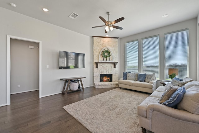 living area featuring dark wood-style floors, recessed lighting, visible vents, a stone fireplace, and baseboards