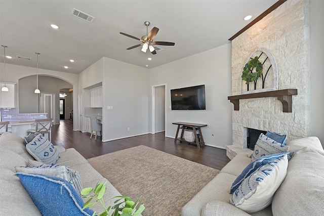 living room featuring visible vents, arched walkways, a ceiling fan, dark wood-style flooring, and a fireplace