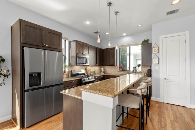 kitchen featuring visible vents, appliances with stainless steel finishes, light stone countertops, dark brown cabinets, and backsplash