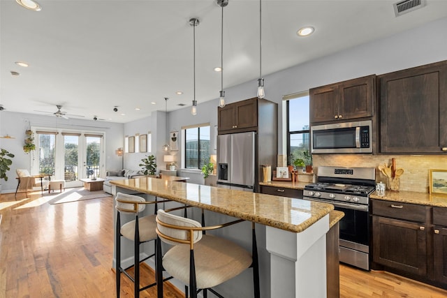 kitchen featuring dark brown cabinetry, stainless steel appliances, visible vents, open floor plan, and a center island